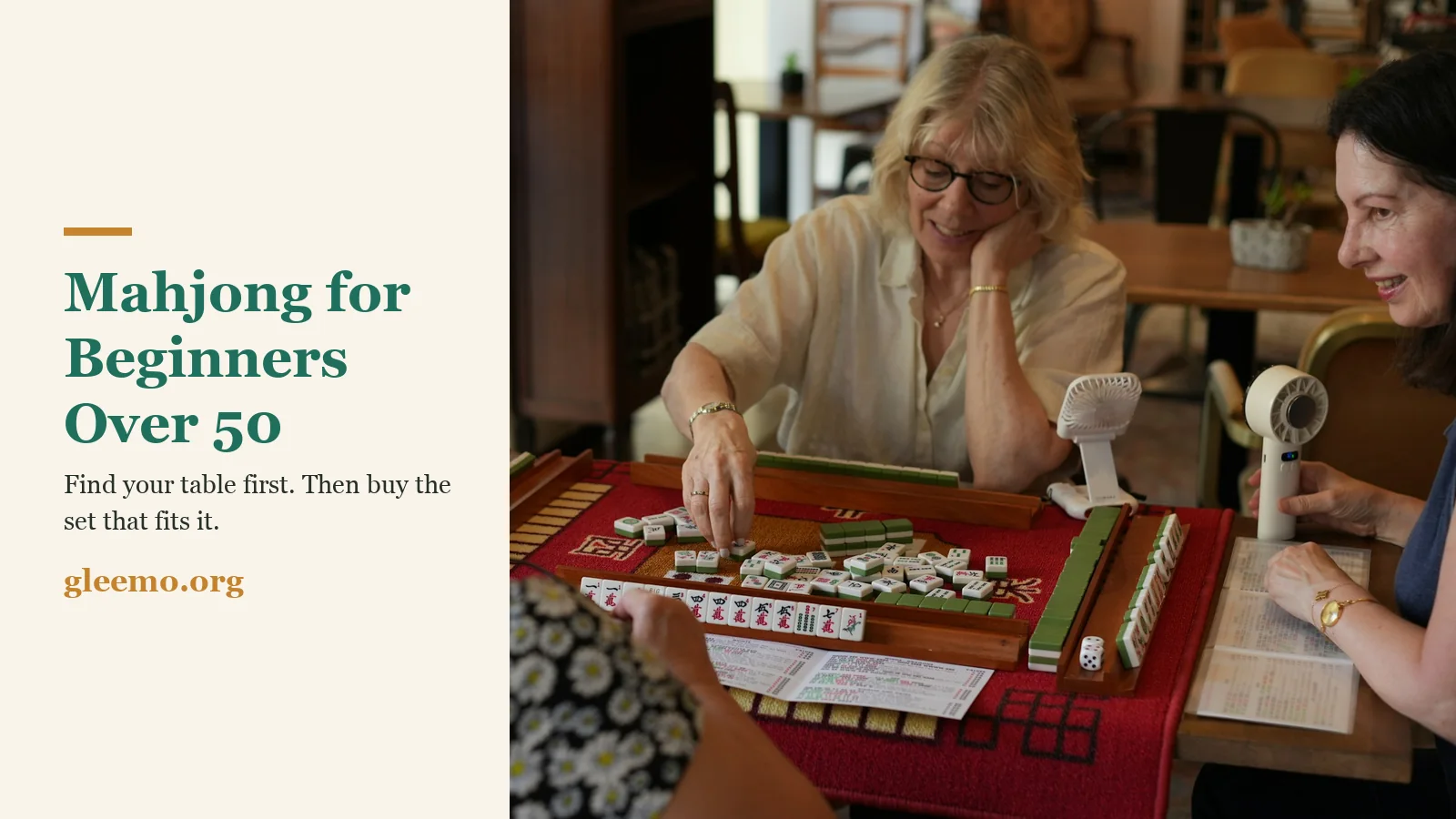 Four women in their 50s to 70s play American mahjong at a cafe table, tiles on wooden racks and the year's card open beside them, with the title Mahjong for Beginners Over 50 and the gleemo.org logo.