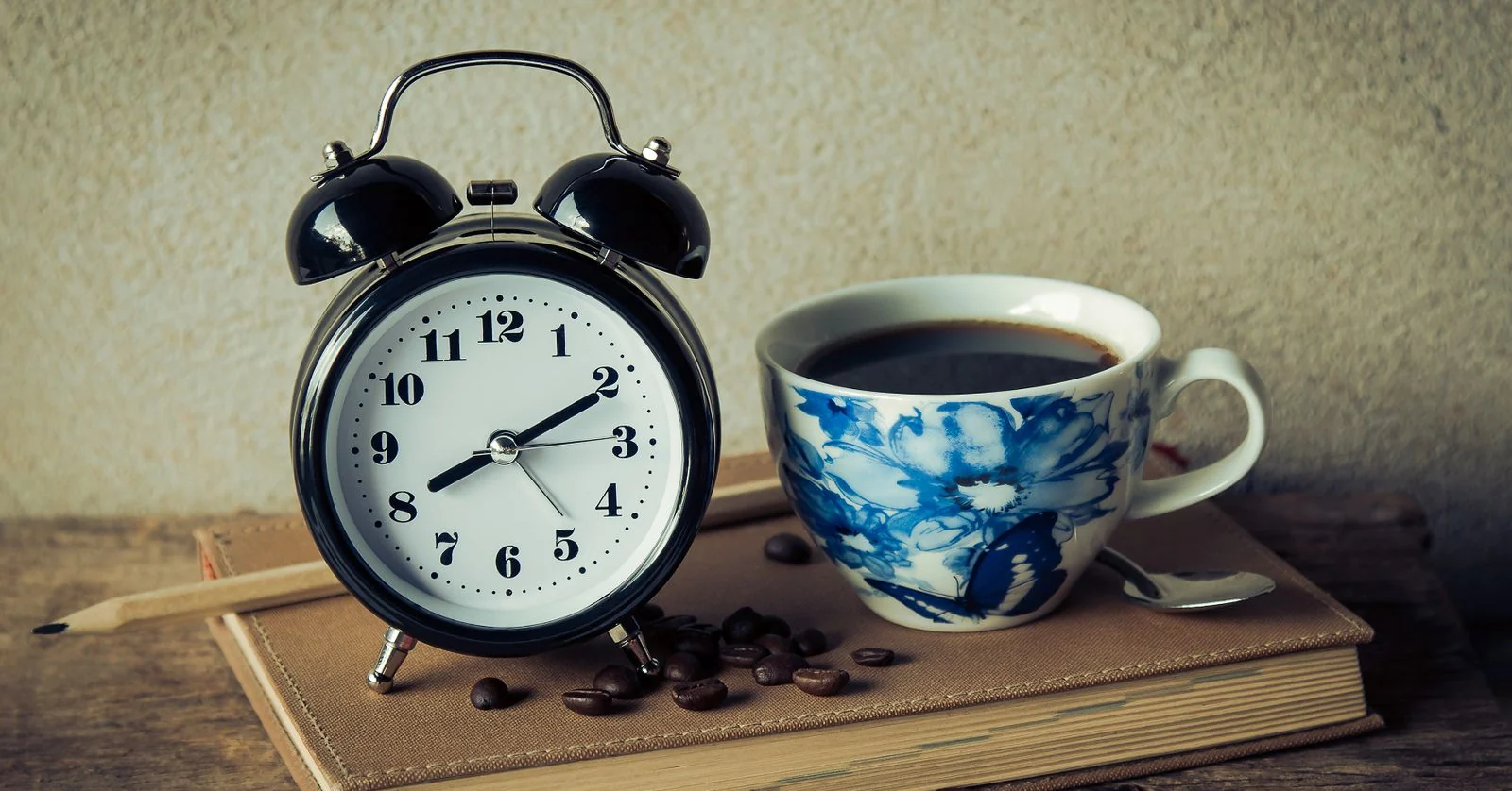 A black alarm clock and a cup of coffee on a book at dawn, ready for an early pre-order morning